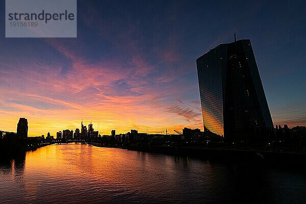 Die Sonne ist hinter der Europäischen Zentralbank (EZB) und der Frankfurter Bankenskyline untergegangen und verfärbt mit ihrem letzten Licht des Tages den Abendhimmel.  Osthafen  Frankfurt am Main  Hessen  Deutschland  Europa