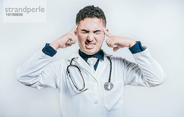Arzt mit Migräne hält seinen Kopf. Erschöpfter Arzt mit Kopfschmerzen isoliert  Junger Arzt mit Kopfschmerzen isoliert