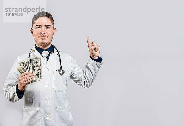 Junger lateinischer Arzt zeigt Geld und zeigt auf die Seite. Fröhlich Arzt hält Geld und zeigt eine Werbung