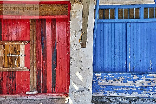 Bunte blaue und rote Bootsgaragentore im Fischerdorf Klima  Insel Milos  Griechenland. Traditionelle weiß getünchte Hauswände  bemalte  verblasste und verwitterte Holztüren und Tore sonniger Sommertag  authentische Architektur und Details. Frontalaufnahme