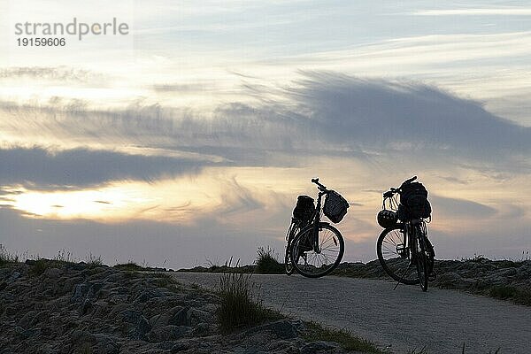 Radtour  Silhouette von Fahrrädern in der Abenddämmerung auf einem Weg am Strand von Cuxhaven  Nordseeküste  Niedersachsen  Deutschland  Europa