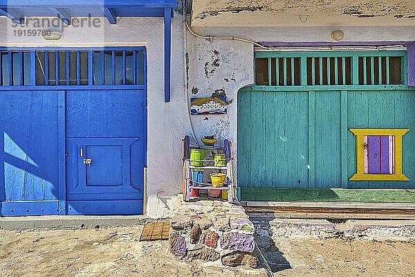 Bunte blaue und grüne Bootsgaragentore im Fischerdorf Klima  Insel Milos  Griechenland. Traditionelle weiß getünchte Hauswand  bemalte  verblasste und verwitterte Holztüren und Tore sonniger Sommertag  authentische Architektur und Details. Frontalaufnahme