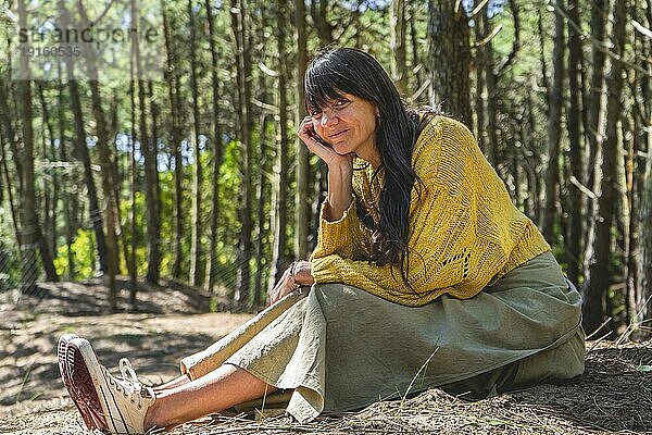 Porträt einer erwachsenen Frau  die in die Kamera schaut  während sie im Wald sitzt