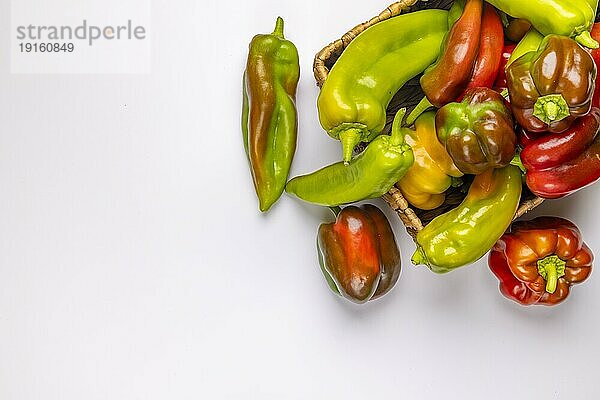 Verschiedene Paprika (Capsicum) in und neben Körbchen  Rot  Grün  Gelb  weißer Hintergrund  Kopierraum