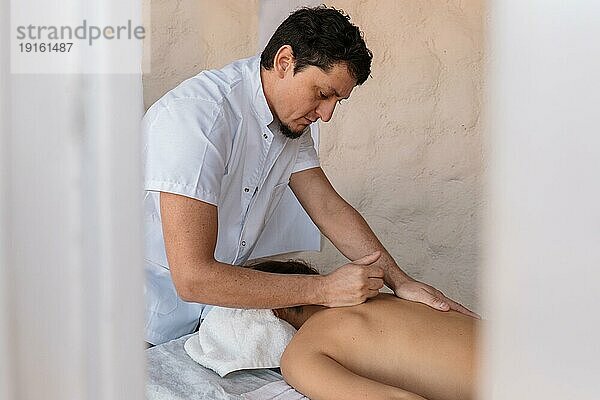 Professionelle männliche Masseur Therapeut führt therapeutische Körpermassage für junge Frau. Massagebehandlung für Stressabbau  Wohlbefinden und Körperharmonie