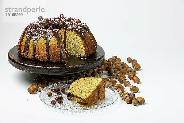 Veganer Haselnusskuchen auf Servierteller aus Holz  angeschnitten  Kuchenstück auf Glasteller  Haselnüsse daneben  weißer Hintergrund  Kopierraum