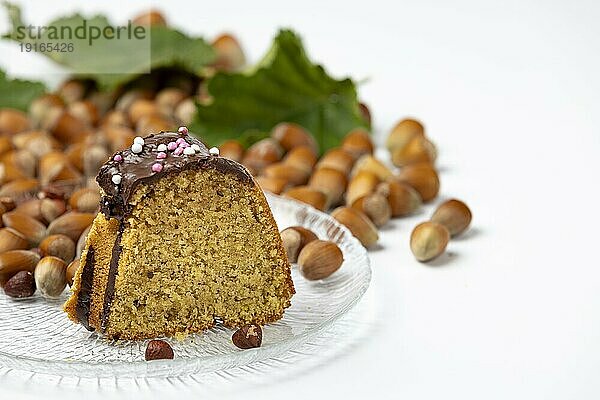 Kuchenstück auf Glasteller  Haselnusskuchen  Haselnüsse und Blätter daneben  weißer Hintergrund  Kopierraum