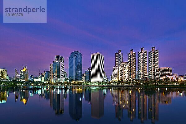 Schöne Landschaft mit modernen Hochhäusern  die sich im ruhigen Wasser des Sees bei farbenfrohem Sonnenuntergang spiegeln. Benjakitti Park  Bangkok  Thailand  Asien