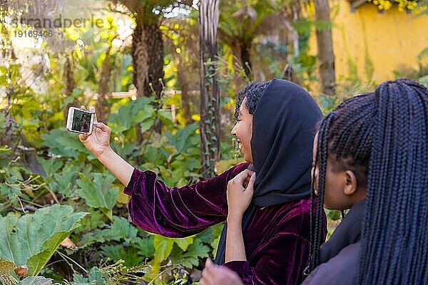 Rückansicht einer muslimischen Frau  die ein Selfie mit Freunden in einem Park macht