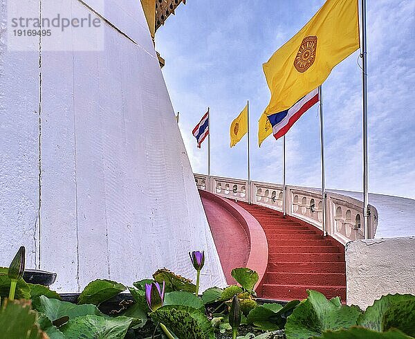 Reihe von thailändischen nationalen  buddhistischen und königlichen Fahnen entlang einer Wendeltreppe mit roten Stufen und weißer Brüstung  Seerosen im unscharfen Vordergrund  selektiver Fokus. Treppe am Golden Mount Tempel oder Wat Saket  Bangkok  Thailand  Asien