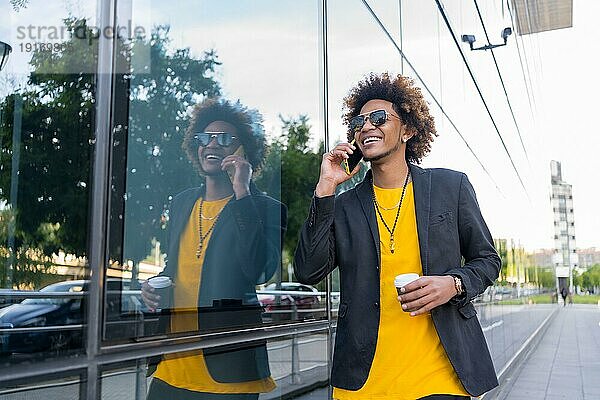 Moderner Geschäftsmann im Gespräch mit dem Handy  der morgens mit einem Kaffee zum Mitnehmen über die Straße geht