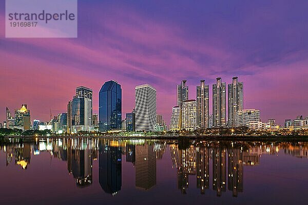 Schöne Landschaft mit modernen Hochhäusern  die sich im ruhigen Wasser des Sees bei farbenfrohem Sonnenuntergang spiegeln. Benjakitti Park  Bangkok  Thailand  Asien