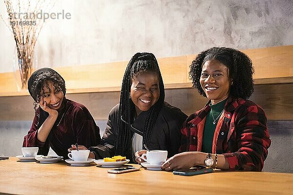 Porträt von drei fröhlichen multikulturellen Freunden beim Kaffeetrinken in einer Cafeteria