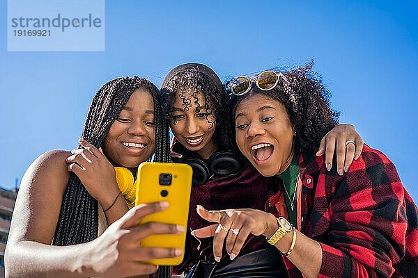 Niedriger Blickwinkel von drei multiethnischen Freunden  die lächelnd ein Handy im Freien benutzen