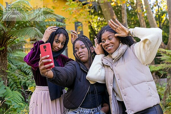 Lustige afrikanische und muslimische Freunde  die Grimassen schneiden und gestikulieren  während sie ein Selfie in einem Stadtpark machen