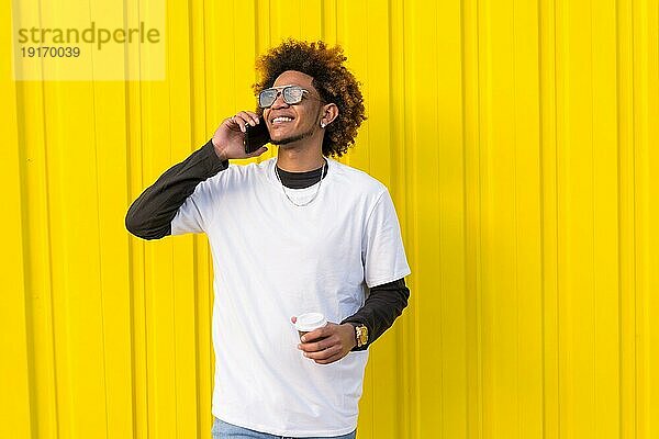 Horizontales Foto mit gelbem Hintergrund eines Mannes mit Afrofrisur im Gespräch mit dem Handy im Freien
