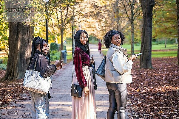 Drei multikulturelle Freunde drehen sich um und lächeln in die Kamera  als sie durch einen Park gehen