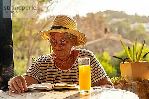Glückliche ältere Frau liest ein Buch auf einer Terrasse mit Blick auf die Natur