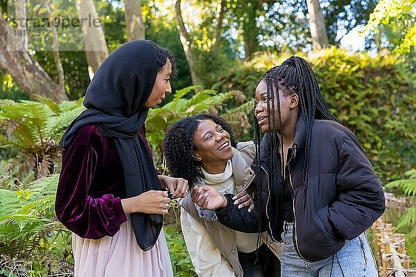 Horizontales Foto einer muslimischen jungen Frau und afroamerikanischer Freundinnen  die in einem Park lachen