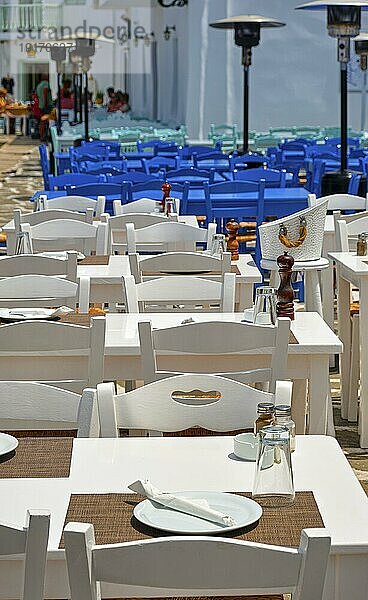 Bunte Tische und Stühle  weiß getünchte Wände von Restaurants  Cafés und Bars in der Bucht von Naoussa  an einem sonnigen Sommertag. Traditionelle griechische Küche  Urlaub  Reiseziel  Touristenparadies  selektiver Fokus  romantisches Essen im Freien im Urlaub