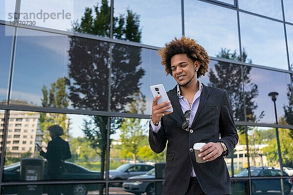 Cooler Geschäftsmann  der während einer Kaffeepause im Freien mit dem Handy telefoniert