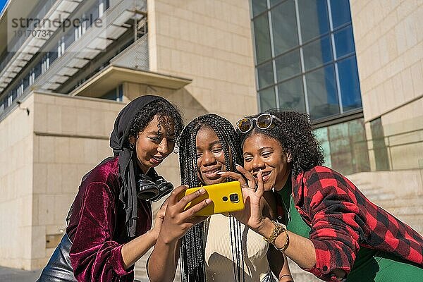 Neugierige multiethnische Freunde benutzen ihr Handy auf der Straße in der Stadt