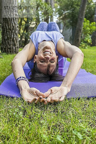 Glücklich lächelnde Frau auf Yoga Blöcken liegend und in die Kamera schauend. Vertikale Aufnahme