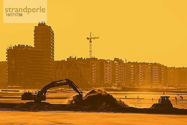 Bulldozer und Hydraulikbagger bei der Verlegung einer Rohrleitung während der Sandauffüllung und der Strandverbesserungsarbeiten bei Sonnenuntergang an den Stränden von Ostende  Belgien  Europa