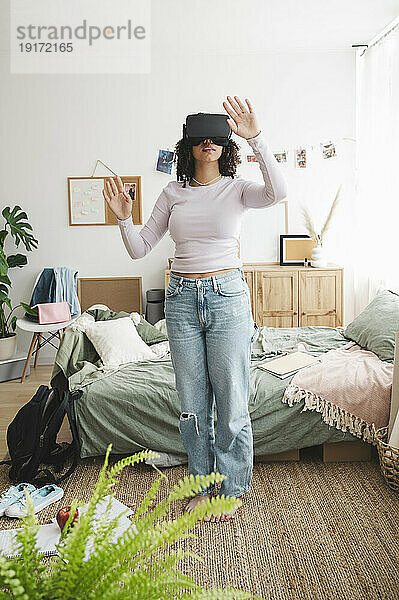 Teenage girl wearing virtual reality simulators gesturing in bedroom at home