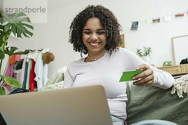 Happy teenage girl with credit card using laptop at home