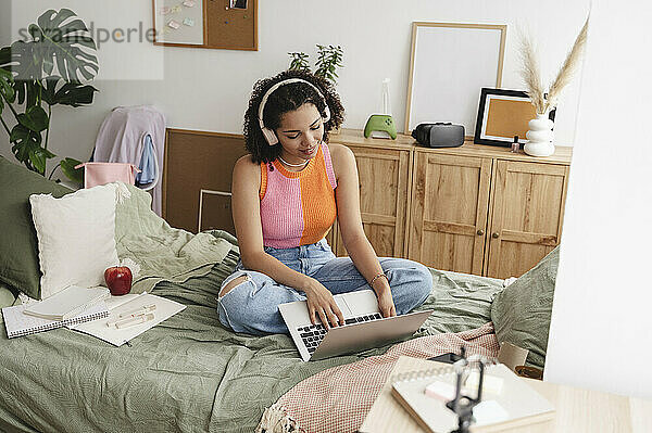 Smiling teenage girl using laptop on bed at home