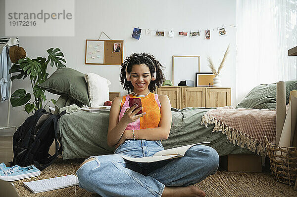 Glückliches Teenager-Mädchen  das zu Hause im Schlafzimmer sein Mobiltelefon benutzt
