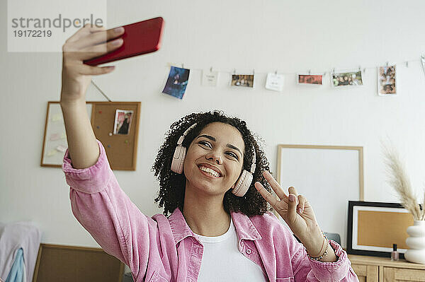 Fröhliches Teenager-Mädchen zeigt ein Friedenszeichen und macht ein Selfie mit dem Smartphone