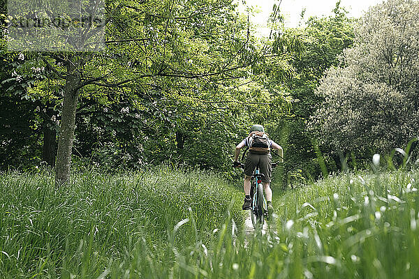 Frau fährt Fahrrad inmitten von Gras im Wald