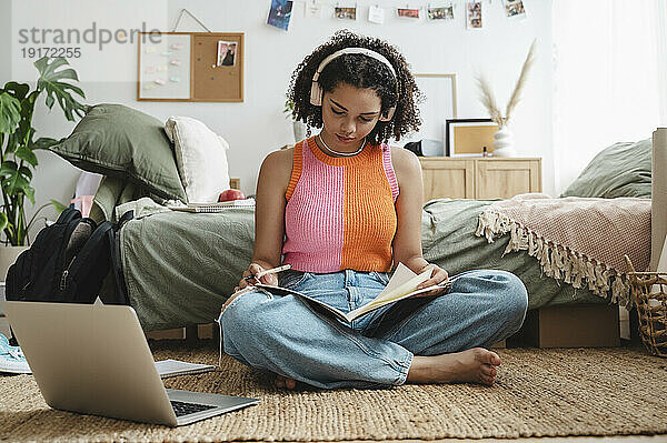 Teenage girl wearing wireless headphones doing homework at home