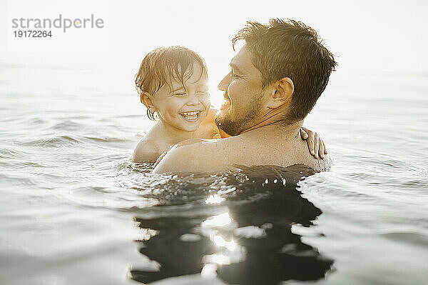 Fröhlicher Vater mit Sohn schwimmt an sonnigem Tag im Wasser