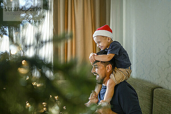 Vater trägt Sohn mit Weihnachtsmütze auf den Schultern und sitzt auf dem Sofa