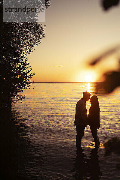 Paar umarmt sich bei Sonnenuntergang vor dem Meer