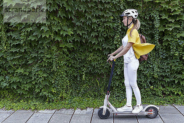 Junge Frau fährt mit Elektroroller vor Pflanzen