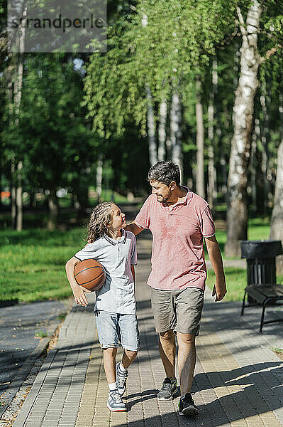 Vater spricht mit Sohn beim Basketball und geht im Park spazieren