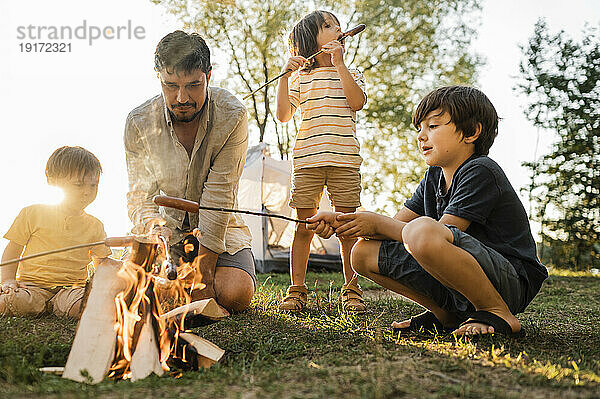 Vater und Kinder braten beim Picknick Würstchen am Lagerfeuer