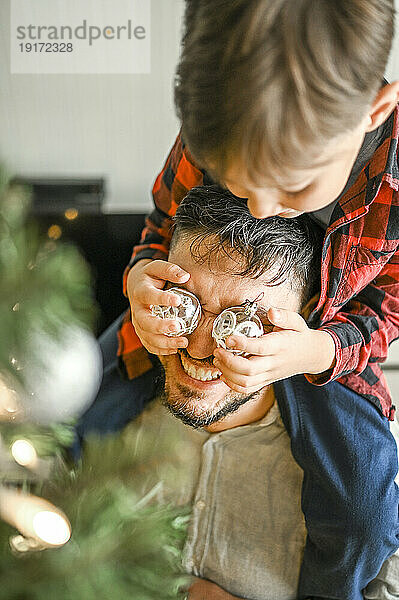 Sohn bedeckt zu Hause die Augen seines Vaters mit Weihnachtslichtern