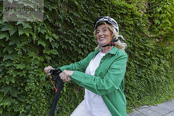 Glückliche ältere Frau mit Helm steht vor Pflanzen