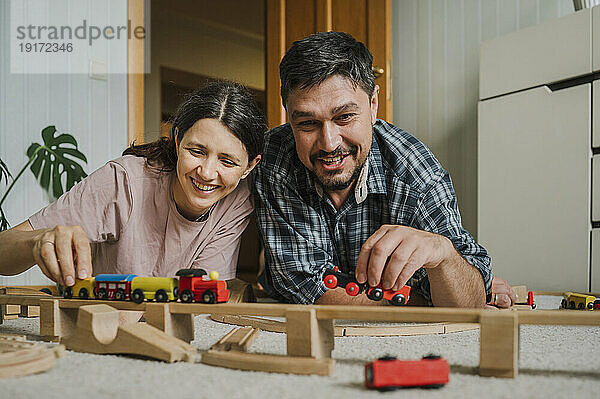 Glückliche Männer und Frauen spielen zu Hause mit der Spielzeugeisenbahn