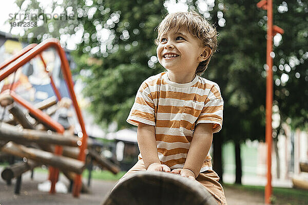 Smiling boy sitting on outdoor play equipment in park