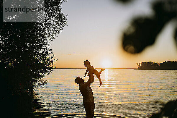 Vater hält Sohn bei Sonnenuntergang vor dem Meer