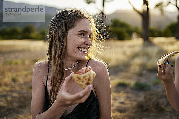 Glückliche Frau  die am Wochenende ein Stück Pizza im Park isst