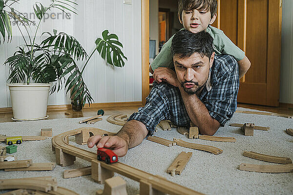 Lächelnder Sohn und Vater spielen zu Hause mit der Spielzeugeisenbahn