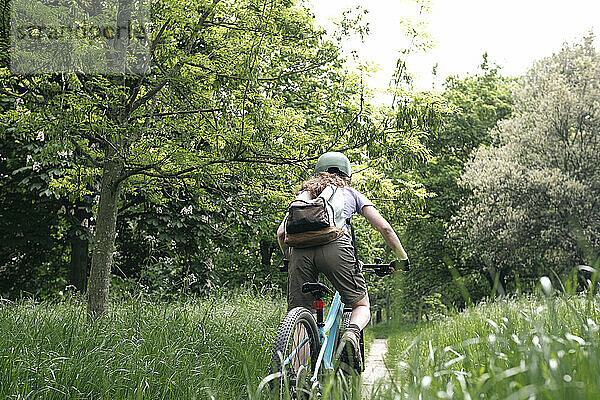 Junge Frau mit Rucksack fährt Fahrrad auf Gras im Wald