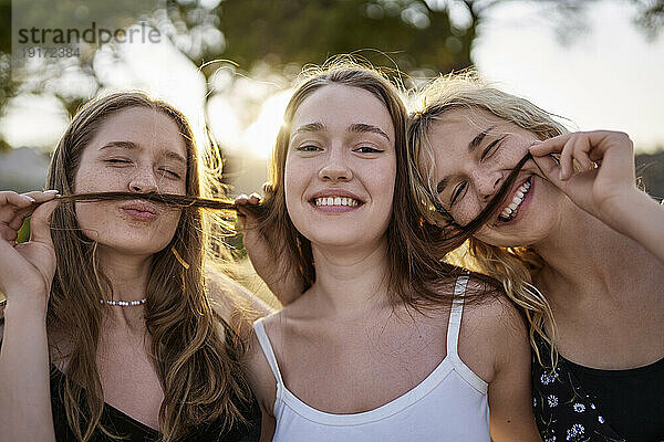 Lächelnde Frauen spielen am Wochenende im Park mit den Haaren einer Freundin